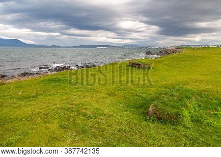 Rocky Coast Of Faxafloi Bay, Town In The Background. Seltjarnarnes, Reykjavik, Iceland.