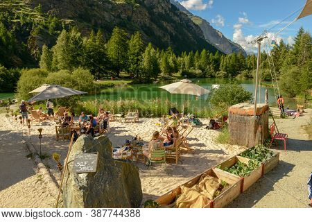 People Drinking In A Beach Bar Of The Lake At Tasch On The Swiss Alps