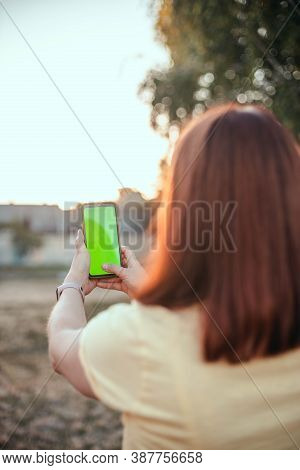 Young Girl With Her Back Makes Selfie On A Smartphone In The Park. Mockup Blank Screen On The Phone,