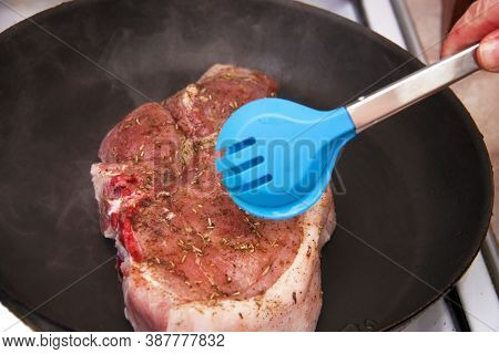 Woman Turning Piece Of Raw Meat By Tongs In A Frying Pan And Steam Around