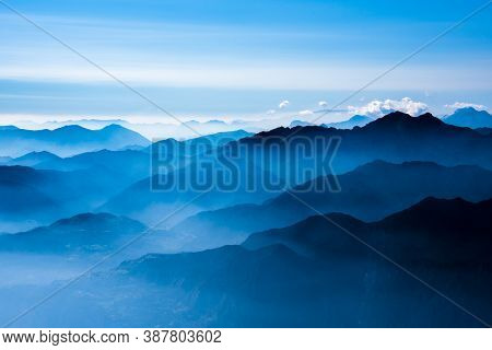 The Peaks Of The Alps Around Lake Garda Surrounded By Fog With Blue Sky Seen From Monte Altissimo, T