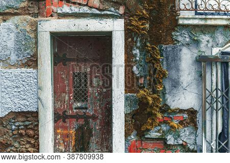 Texture Of An Old Flaked Stone Facade Wall Of An Antique House With A Doorway, Red Bricks, Stones, A