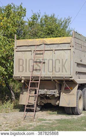 Ladder At The Rear Of A Dump Truck On The Side Of The Road. Truck With High Sides And A Closed Awnin