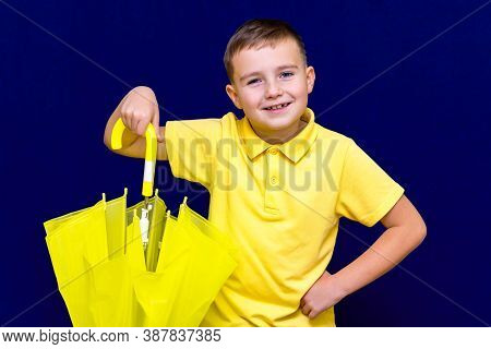 Attractive Surprised Caucasian Blond Schoolboy Holds Unexpanded Umbrella On Blue Studio Background.b