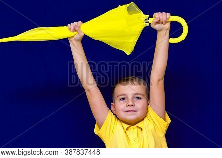 Attractive Surprised Caucasian Blond Schoolboy Holds Unexpanded Umbrella On Blue Studio Background.b