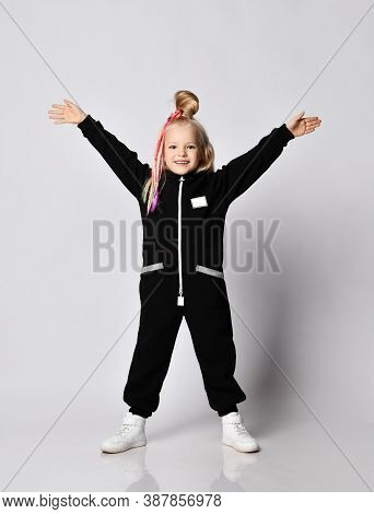 Cheerful Blonde Kid Baby Girl With Colorful Braids Wearing Stylish Black Jumpsuit With Hood And Pock