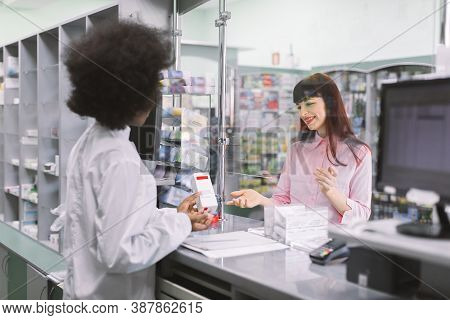 Back Angle View Of Female Afrcian Pharmacist Giving Medicine To Young Smiling Caucasian Woman In Dru