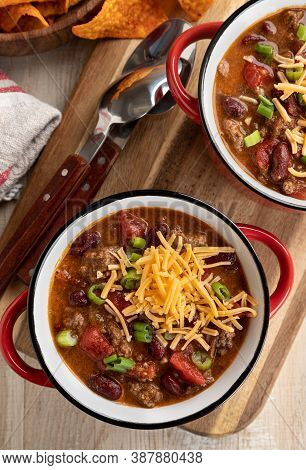 Bowl Of Chili Con Carne With Shredded Ceddar Cheese On A Rustic Wooden Table.  Overhead View