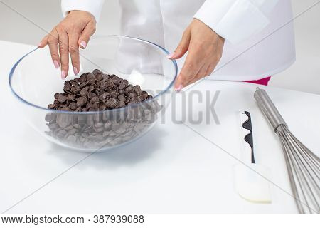 Female Chocolatier Keeps Dark Chocolate Couverture Callets In Glass Pot. Chocolate Drops For Prepara