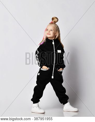 Smiling Blonde Kid Baby Girl With Colorful Braids Wearing Stylish Black Jumpsuit And Sneakers Side T