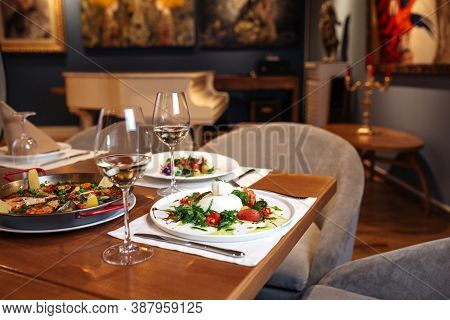 Restaurant Table Served With Spanish Buratta Tomato And Peppers Salads And Paella