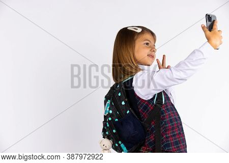 Photo Of Joyful Beautiful Schoolgirl Taking Selfie On Cellphone And Gesturing Peace Sign Isolated Wh