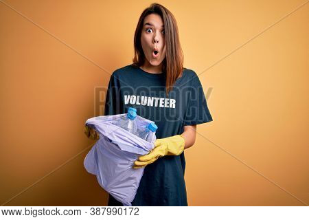 Beautiful volunteer girl caring environment doing volunteering holding bag with rubish bottles scared in shock with a surprise face, afraid and excited with fear expression