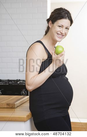 부엌에서 행복 한 임신 여자 먹는 애플의 초상화