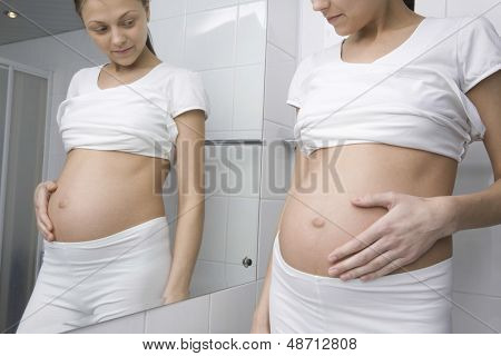 욕실 거울 앞에 서 있는 젊은 임산부의 중앙부
