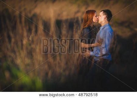 couple kissing standing outdoos among bushes