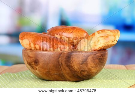Empanadillas al horno frescos, en un recipiente de madera, en la mesa de madera, sobre fondo brillante