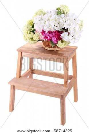 Wicker basket with flowers on small wooden ladder, isolated on white