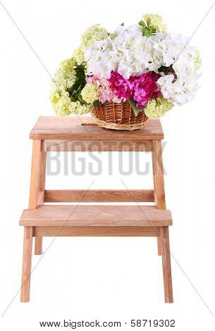 Wicker basket with flowers on small wooden ladder, isolated on white