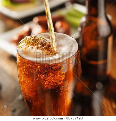 pouring beer into glass with bbq chicken wings in background
