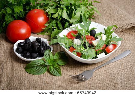 Greek Salad In White Salad Bowl With Cutlery And Vegetables Around