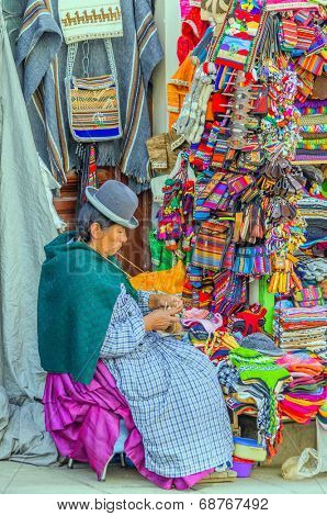 LA PAZ, BOLIVIA, MAY 9, 2014 - Local woman in traditional costume and bowler hat sits in front of her souvenir stand, knitting