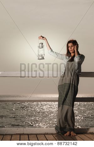 Young Woman On Pier With Oil Kerosene Lamp.