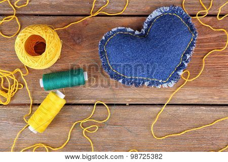 Denim heart and thread on wooden background
