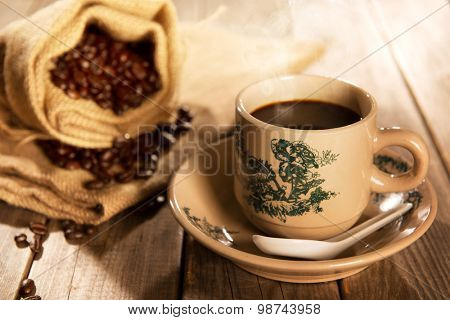 Steaming traditional oriental Chinese kopitiam style dark coffee in vintage mug and saucer with coffee beans. Fractal on the cup is generic print. Soft focus with dramatic light on wooden background.
