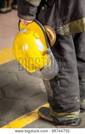 Low section rear view of fireman holding helmet at fire station