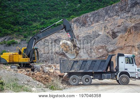 excavator puts a huge stone in the truck