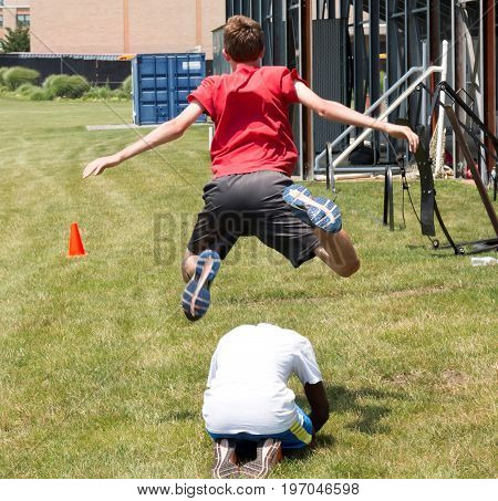 A high school kid plays leapfrog behind the bleachers on the grass at the end of practice