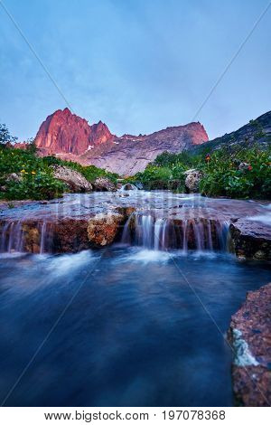 Sunset in mountains near river. Sunlight reflected on mountain tops. Golden light from sky reflected in a mountain river. Ergaki