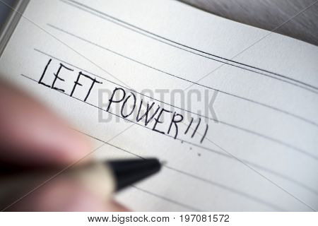 closeup of a young left-handed man handwriting the text left power in a notepad