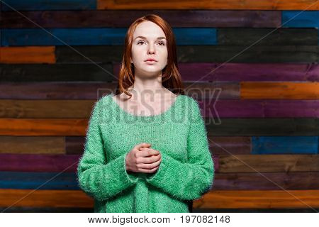 beautiful girl with red hair in greem pullover over colorful wooden background. beauty model woman with luxurious red hair. hairstyle. holiday makeup
