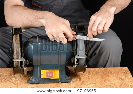 A man in working clothes hones professional sharpening kitchen knive on the table more horizontal knife