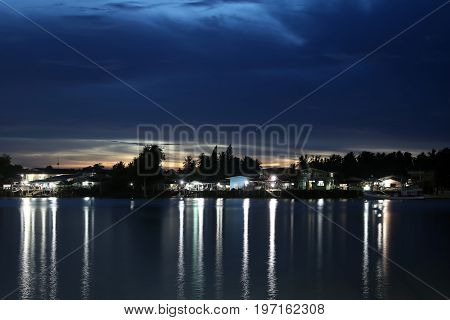 Riverside village with lights at night in Thailand.