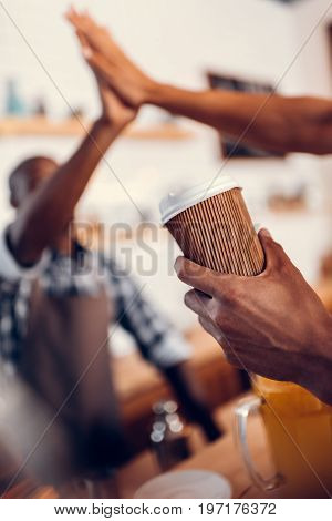African American Barista Giving Highfive To Client With Disposable Cup In Coffee Shop