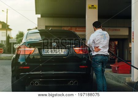 PARIS FRANCE - MAY 7 2016: Adult man refueling at the gas station his BMW X6 M sport suv with sun flare light leak