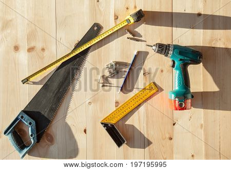 Electric screwdriver roulette and handsaw at wooden desk background
