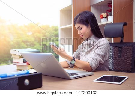 Portrait of a beautiful businesswoman working on her laptop and using hands modern Smart phone while sitting at officePeople Working Together Project.