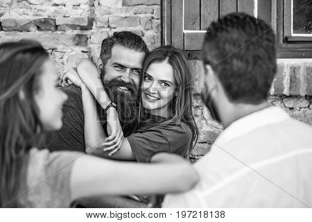 Couple of handsome bearded men with long beard and stylish hair and blonde pretty cute sexy woman or girl embracing and smiling to they friends on summer sunny day on stony wall background