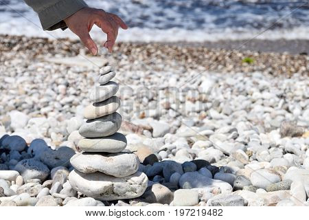 Female puts the last stone on top of a stone tower on the beach