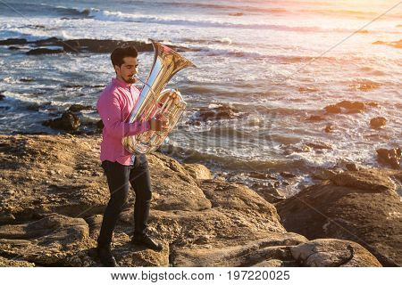 Young musician play the Tuba on rocky sea coast during surf. Trumpet. 