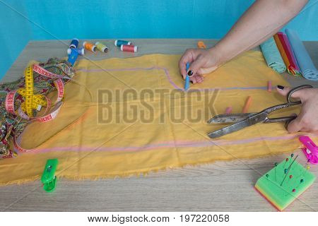 Close up of woman's hands drawing a pattern on yellow tissue. Measuring tape and sewing accessories. A tailor is laying out a dress/Sewing layout