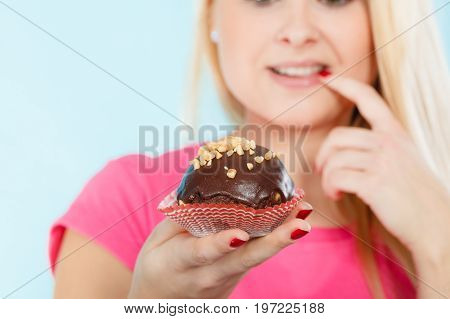 Diet sweets food concept. Woman holding delicious chocolate cupcake with peanut frosting about to take bite