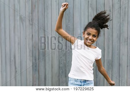 Happy girl jumping near a wall outdoors