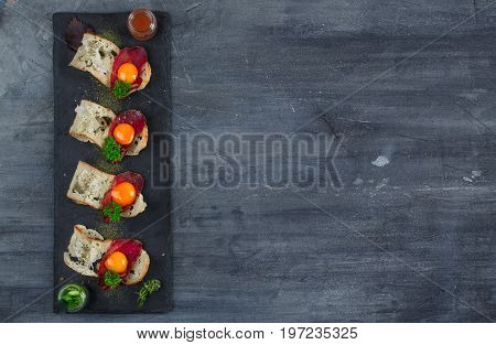 Four tiny appetizers with cured met, yolk and parmegano cheese on stone board with copyspace. Top view.