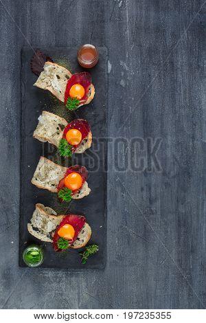 Four tiny appetizers with cured met, yolk and parmegano cheese on stone board with copyspace. Top view.