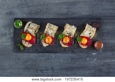 Four tiny appetizers with cured met, yolk and parmegano cheese on stone board with copyspace. Top view.